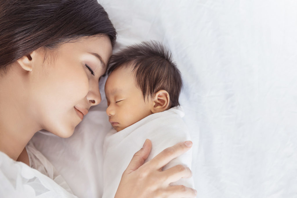 Close up portrait of beautiful young asian or caucasian mother girl kissing her healthy newborn baby sleep in bed with copy space. Healthcare and medical love asia woman lifestyle mother’s day concept
